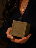 Hand holding an artisanal Savon de Marseille soap cube, labeled extra pure 72% oil.