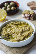 Tapenade verte de Provence dans un bol, accompagnée d’olives, citron et pain artisanal